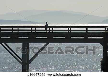 Stock Photo - Silhouette of a man walking along a pier, Sidney, BC, Canada. Fotosearch