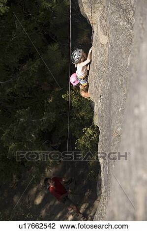 Stock Image - Young woman climbing with daughter (age 7) up granite cliff while husband/father belays, Stone Hills near Rexford, Montana, USA. Fotosearch