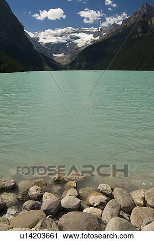Stock Image - Alpine lakeshore with glacier capped mountains in the background, Lake Louise, Banff National Park, Alberta, Canada. Fotosearch