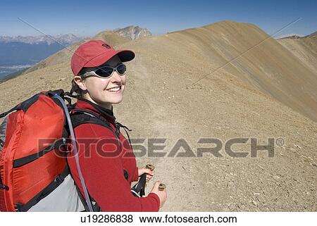 Stock Photo - A woman (20-25) smiles while hiking in the alpine; Canada, Alberta, Jasper National Park, Skyline Trail. Fotosearch