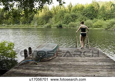 Stock Image - Woman (20-25) walking across a dock with a rowboat on it in a swimsuit, Victoria, Vancouver Island, B. C.. Fotosearch