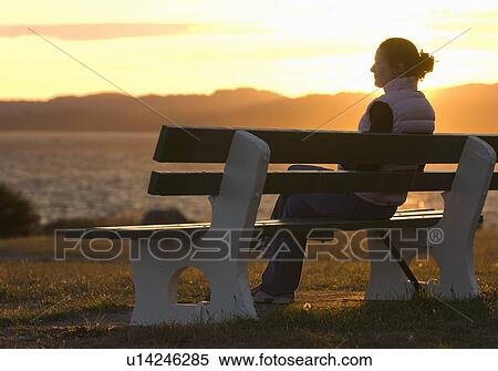 Stock Photography - A woman enoys the sunset from a park bench along Victoria's Dallas Road Waterfront. Fotosearch