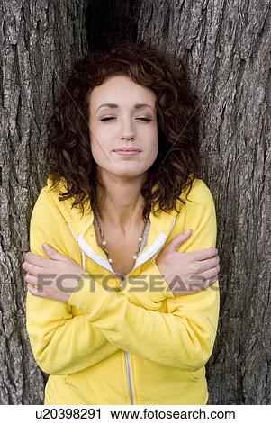 Stock Image - Woman with eyes closed leans against trunk of tree, Munson Park, Winnipeg, Canada. Fotosearch