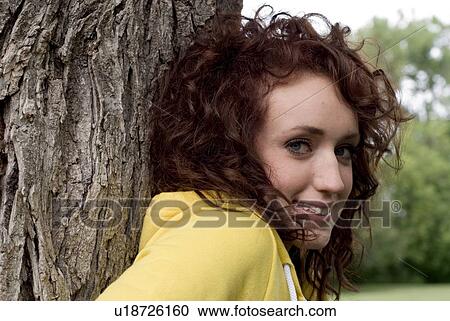 Stock Image - Young woman leaning against large tree, Munson Park, Winnipeg, Canada. Fotosearch