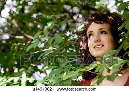 Stock Image - Young woman's face surrounded by green leaves, Munson Park, Winnipeg, Canada. Fotosearch