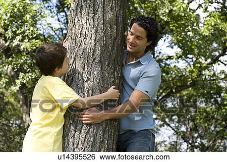 Stock Photograph - Six year old boy and father hugging tree, Assiniboine Park, Winnipeg, Canada. Fotosearch