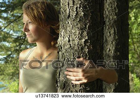 Stock Image - Woman with arm around tree, in a grove of trees, Riding Mountain National Park, Manitoba, Canada. Fotosearch
