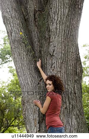 Stock Photo - Young woman stands beside trunk of large tree, Munson Park, Winnipeg, Canada. Fotosearch