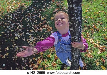 Stock Photograph - Girl, 4, catches leaves as they fall from tree, trunk visible, Whistler, BC. Fotosearch
