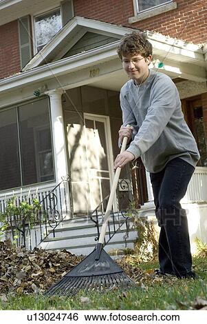 Stock Photograph - Teen boy listening to music while raking, Winnipeg, Canada. Fotosearch
