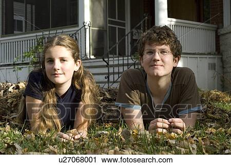 Stock Image - Teen brother and sister lying in leaves, Winnipeg, Canada. Fotosearch