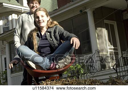 Picture - Teen brother carrying sister in wheelbarrow, Winnipeg, Canada. Fotosearch