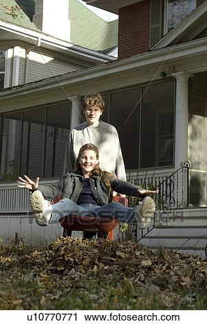 Stock Image - Teen brother carrying sister in wheelbarrow, Winnipeg, Canada. Fotosearch