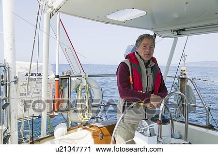 Stock Image - Man at the helm of a sailboat off the coast of California near San Francisco. Fotosearch
