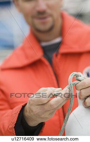 Man in marine rain/floatation gear tieing knot, Vancouver, B. C. View Large Photo Image Stock Photo - Man in marine rain/floatation gear tieing knot, Vancouver, B. C.. Fotosearch