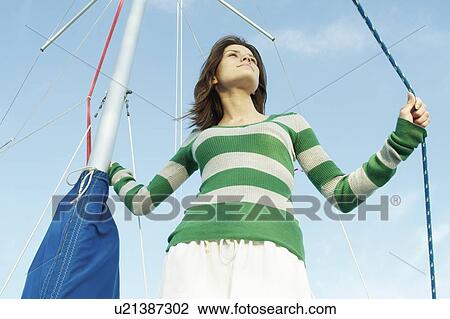 Stock Image - Woman with hand on mast and rope on sailboat, Clear Lake, Riding Mountain National Park, Manitoba, Canada. Fotosearch