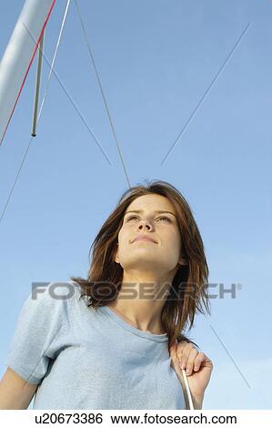 Stock Photograph - Young woman looking upward, on sail boat, wearing hemp shirt, Clear Lake, Riding Mountain National Park, Manitoba, Canada. Fotosearch