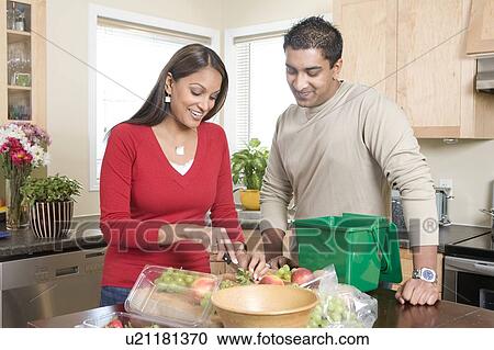 Stock Image - Couple cutting up fruit in kitchen, beside kitchen compost bin. Strawberrries container is made from compostable corn-based product, Winnipeg, Canada. Fotosearch