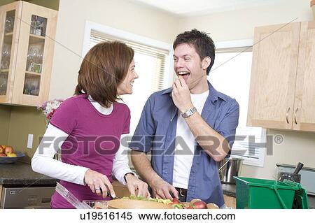 Stock Photography - Couple cutting up fruit in kitchen, beside kitchen compost bin. Strawberrries container is made from compostable corn-based product, Winnipeg, Canada. Fotosearch