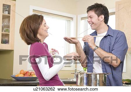 Stock Image - Man offers spoon for woman to taste, Winnipeg, Canada. Fotosearch