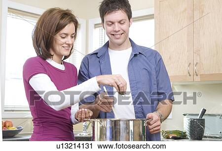 Stock Image - Man stirs as woman sprinkles fresh herbs into pot, Winnipeg, Canada. Fotosearch
