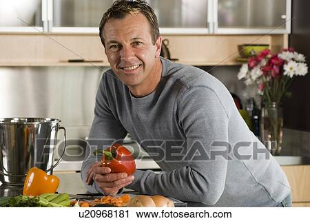 Stock Image - Man with vegetables in kitchen, with metal kitchen compost pail for collecting kitchen scraps, Winnipeg, Canada. Fotosearch