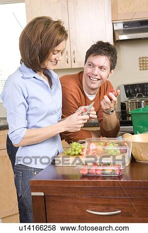 Stock Photo - Woman cutting up fruit, man beside kitchen compost bin, Winnipeg, Canada. Fotosearch