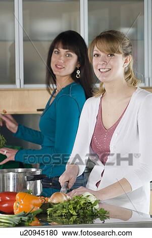 Stock Image - Woman cutting vegetables, other woman puts vegetable scraps into kitchen compost pail, Winnipeg, Canada. Fotosearch