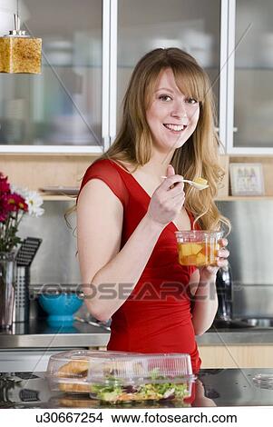 Picture - Woman eating take out food from containers and spoon made from corn, and which are fully compostable, Winnipeg, Canada. Fotosearch
