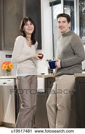 Stock Image - Woman holds organic apple in kitchen, with man. Home has recovered/recycled cupboards and hardwood floors, Winnipeg, Canada. Fotosearch