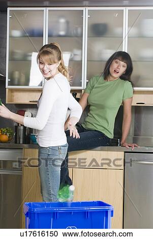 Stock Image - Woman tossing recyling into recycling bin as friend watches, Winnipeg, Manitoba. Fotosearch