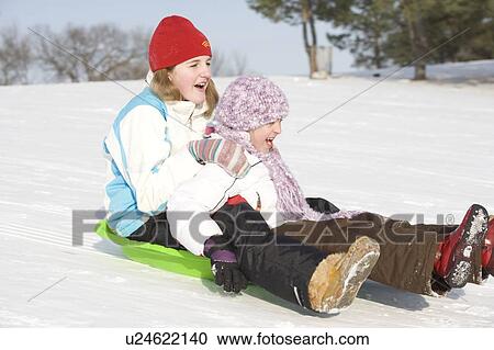 Stock Image - 13 and 9 year olds slide down hill, Winnipeg, Canada. Fotosearch