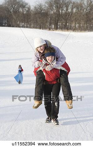 Picture - 15 year old piggy-backs 13 year old girl up hill, outdoor winter, Winnipeg, Canada. Fotosearch