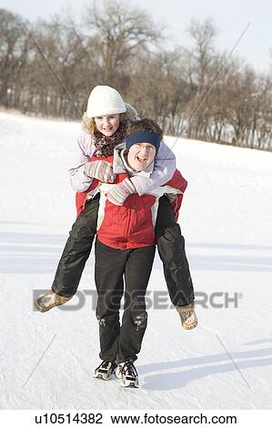Stock Image - 15 year old piggy-backs 13 year old girl up hill, outdoor winter, Winnipeg, Canada. Fotosearch