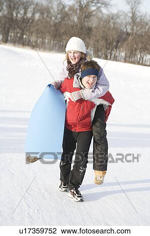 Stock Image - 15 year old piggy-backs 13 year old girl up hill, outdoor winter, Winnipeg, Canada. Fotosearch
