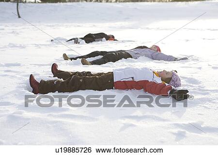 Stock Photograph - 3 kids, (14, 13, and 9 years old) lying on snow, making snow angel, Winnipeg, Canada. Fotosearch