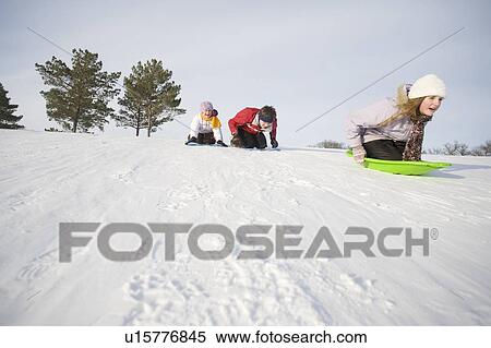 Stock Photography - 3 kids (14, 13 and 9 years old) sliding down hill, Winnipeg, Canada. Fotosearch
