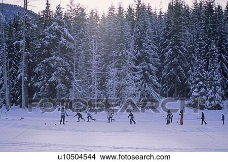 Men play hockey on mountain lake, winter late day, Whistler, B. C. View Large Photo Image Picture - Men play hockey on mountain lake, winter late day, Whistler, B. C.. Fotosearch