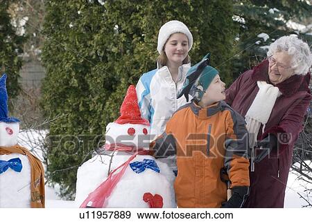 Stock Photo - Senior woman with two children beside snowmen, Winnipeg, Canada. Fotosearch