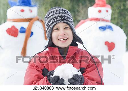Stock Image - Ten year old boy holding snow, beside snowmen, Winnipeg, Canada. Fotosearch