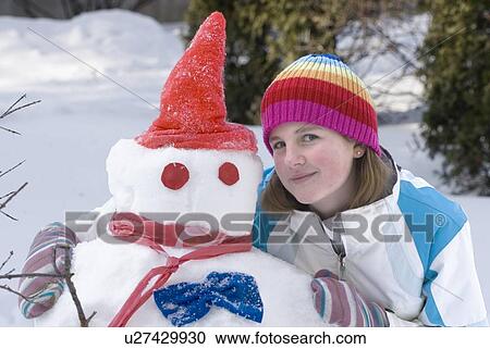 Stock Image - Thirteen year old girl beside snowman, Winnipeg, Canada. Fotosearch