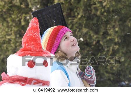 Stock Image - Thirteen year old girl looking upward, beside snowman, Winnipeg, Canada. Fotosearch