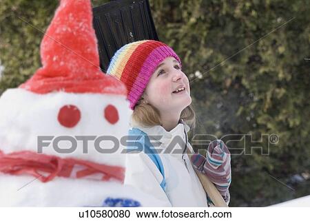Stock Image - Thirteen year old girl looking upward, beside snowman, Winnipeg, Canada. Fotosearch