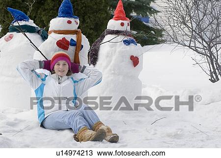 Stock Image - Thirteen year old girl relaxing beside snowmen, Winnipeg, Canada. Fotosearch