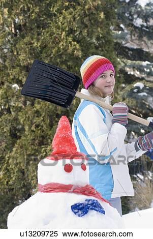 Stock Photography - Thirteen year old girl with shovel beside snowmen, Winnipeg, Canada. Fotosearch