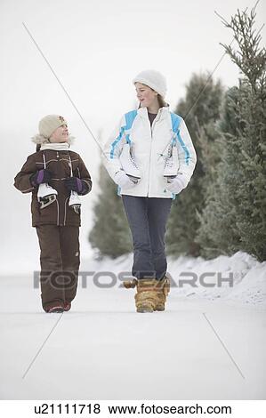 Stock Photo - Two girls (9 and 13) with skates walking along frozen Assiniboine River skating trail, Winnipeg, Canada. Fotosearch