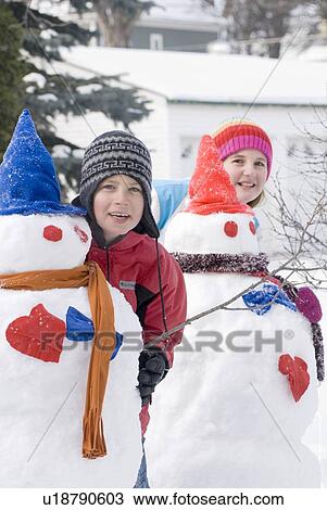 Stock Image - Young boy and girl standing behind snowmen, Winnipeg, Canada. Fotosearch
