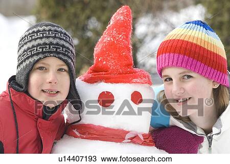 Stock Image - Young girl and boy beside snowman, Winnipeg, Canada. Fotosearch