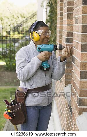 Stock Photo - African American woman using a hand drill, Vancouver, BC. Fotosearch