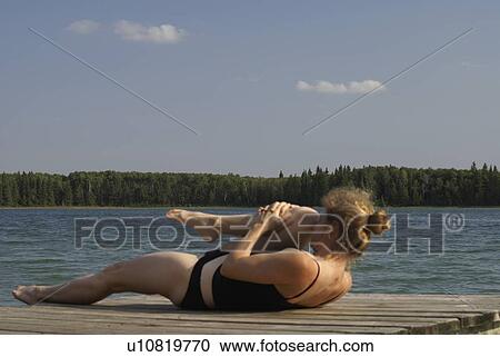 Stock Image - 45 year old woman doing yoga on dock, no motors allowed on lake.; Canada, Manitoba, Riding Mountain National Park. Fotosearch